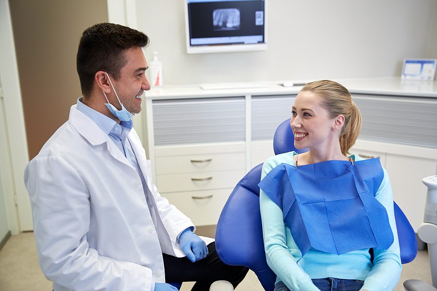 Male dentist in a white lab coat talking to female patient. 