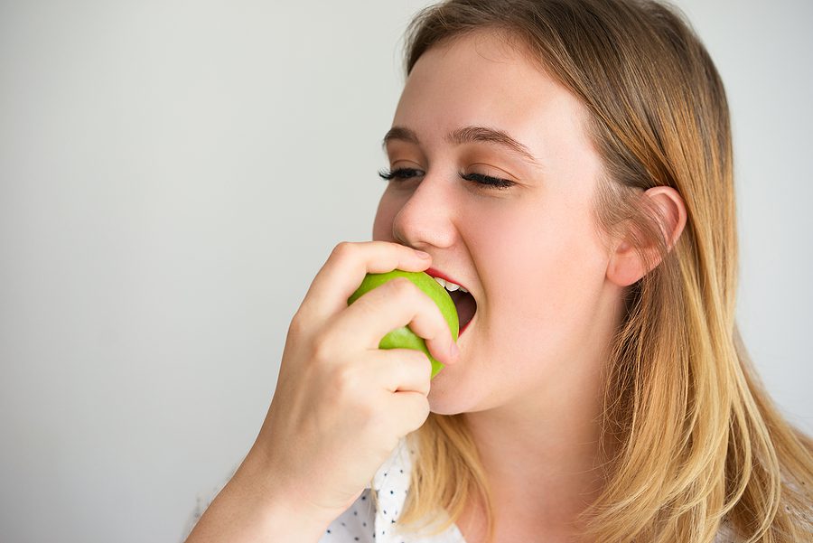 Young female dental patient, eating an apple and satisfied with her recent dental procedure. 